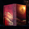 Load image into Gallery viewer, A hardcover journal titled '13 MOON JOURNAL 2027' displayed open to show the front cover, spine, and inner cover. The cover features a cosmic design with a glowing sun, stars, and mountain silhouettes in deep red, burgundy, and gold tones, set against a dark background with subtle smoke.
