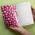 Load image into Gallery viewer, Notebook with floral cover and calendar page held by a hand on a green background
