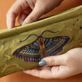 Load image into Gallery viewer, Embroidered clutch with a moth design held by hands against an orange background
