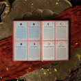 Load image into Gallery viewer, An open booklet or card set laid flat on a decorative brass tray with draped red fabric and warm fairy lights. The booklet has six pink-bordered panels with moon phase headings and small circular moon illustrations.
